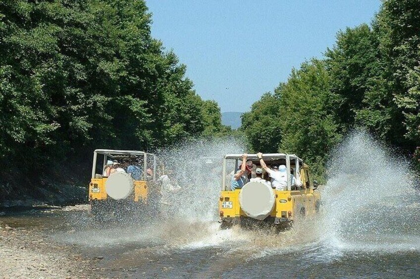 Two yellow jeeps driving through a river, creating splashes. 5