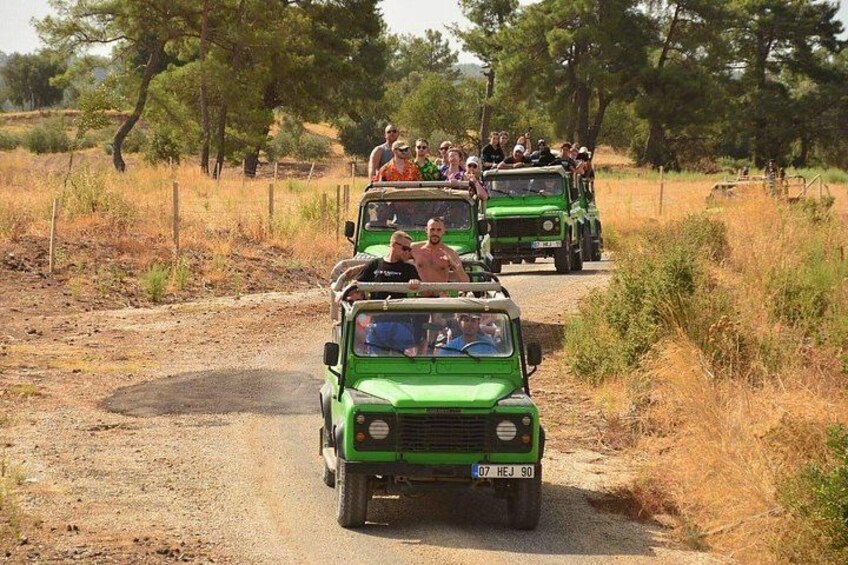 A convoy of green off-road vehicles on a dirt road surrounded by dry grass and trees. 3