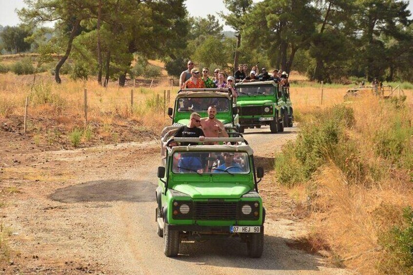 A convoy of green off-road vehicles on a dirt road surrounded by dry grass and trees. 3