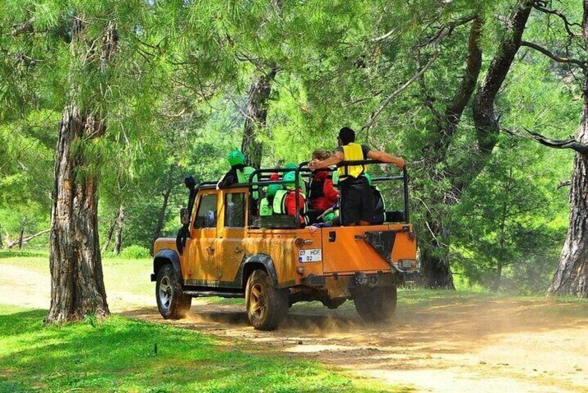A yellow off-road vehicle with passengers, driving on a dirt road through a forest. 4