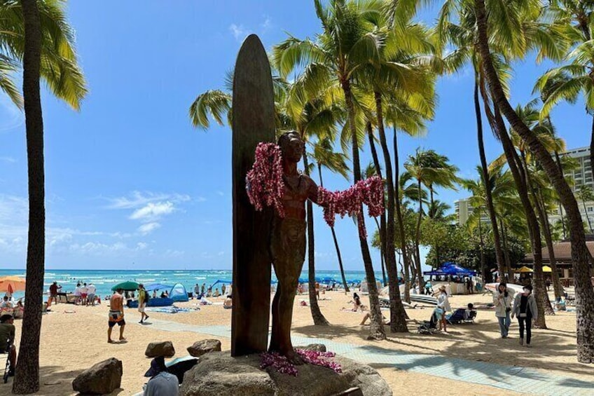 A beach with palm trees, a surfboard sculpture, and people sunbathing. 2