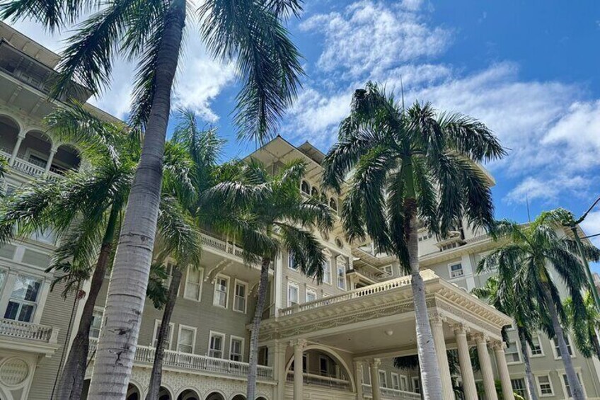A multi-story building with a grand entrance, palm trees, and a clear blue sky. 3