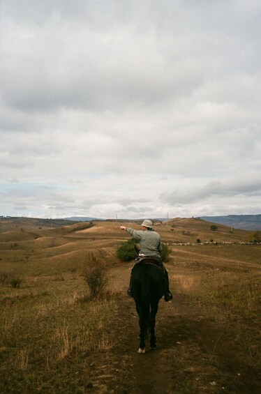 A person riding a horse on a dirt path through a hilly landscape. 3