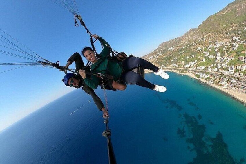 Two people paragliding over a coastal area with clear blue waters and a distant town. 5