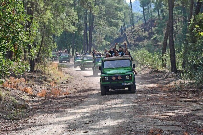 A convoy of green off-road vehicles on a dirt road surrounded by trees. 4
