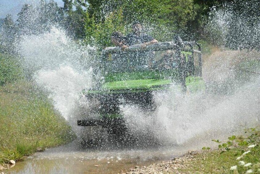 A vehicle driving through a shallow water crossing, creating a spray of water. 3