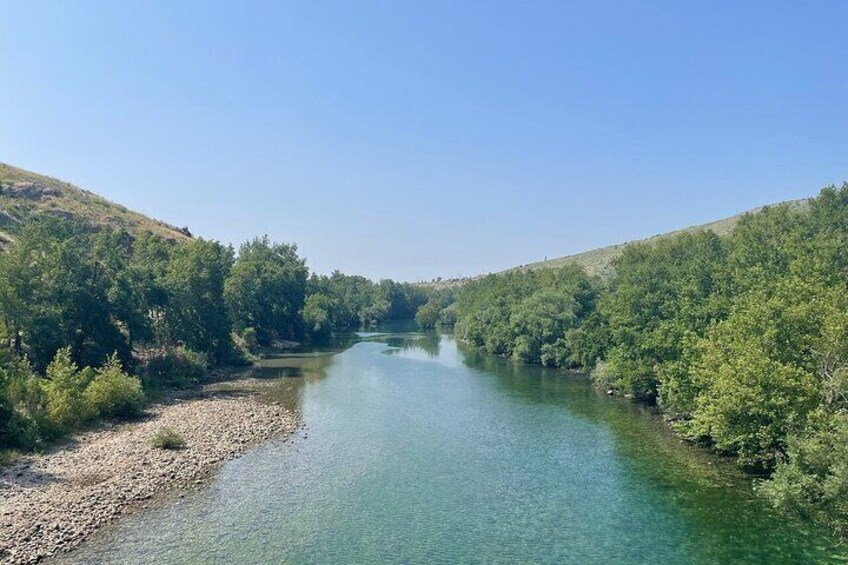 A river flanked by dense green trees under a clear sky. 3