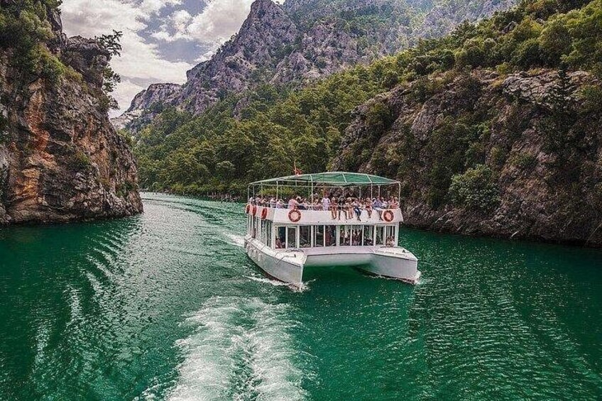 A boat with passengers on a river surrounded by rocky cliffs and greenery. 1
