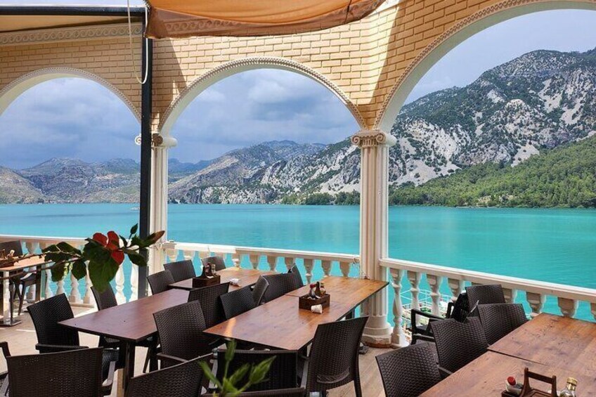 An outdoor seating area with tables and chairs overlooking a turquoise lake and mountains. 2