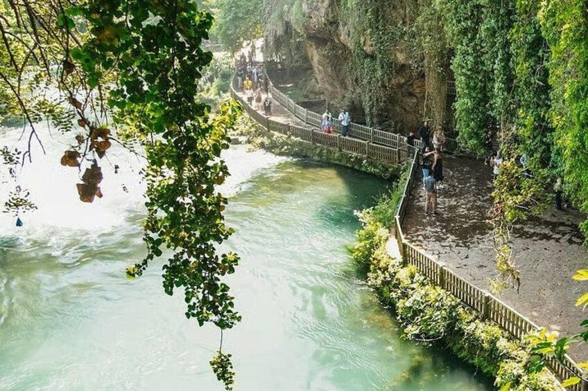 A river with a wooden walkway, surrounded by greenery and rocky cliffs. 4
