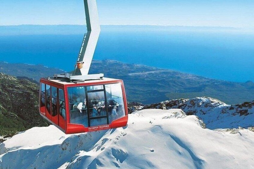 A red cable car on a snowy mountain with a clear view of the ocean in the background. 2