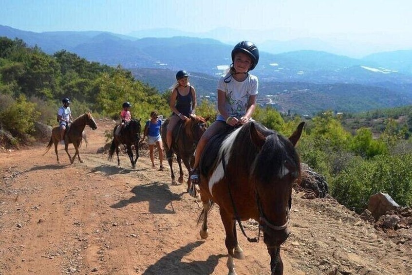 A group of people riding horses on a dirt path with a mountainous landscape in the background. 5