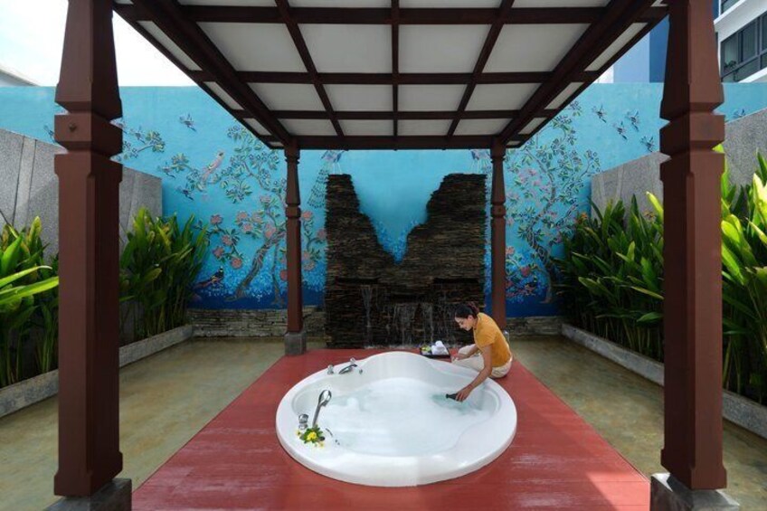 A person cleaning a white bathtub under a wooden pergola with a mural of fish and coral in the background. 3