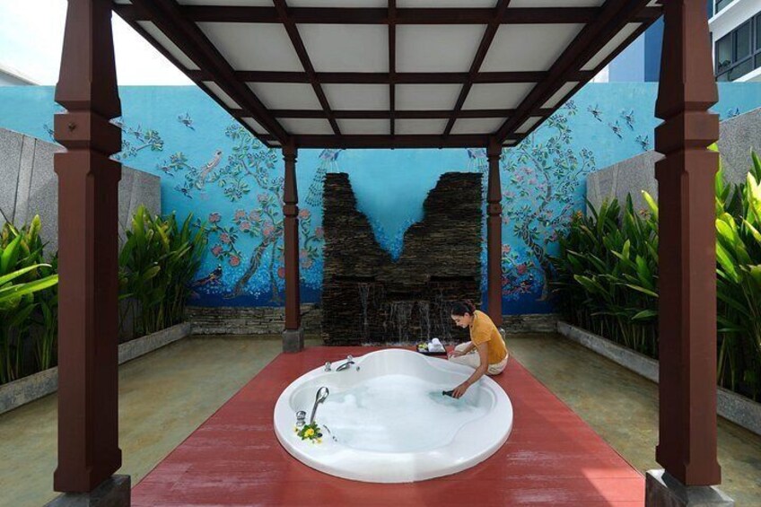 A person in a yellow shirt cleaning a white bathtub under a wooden pergola with a mural of fish and a waterfall. 3