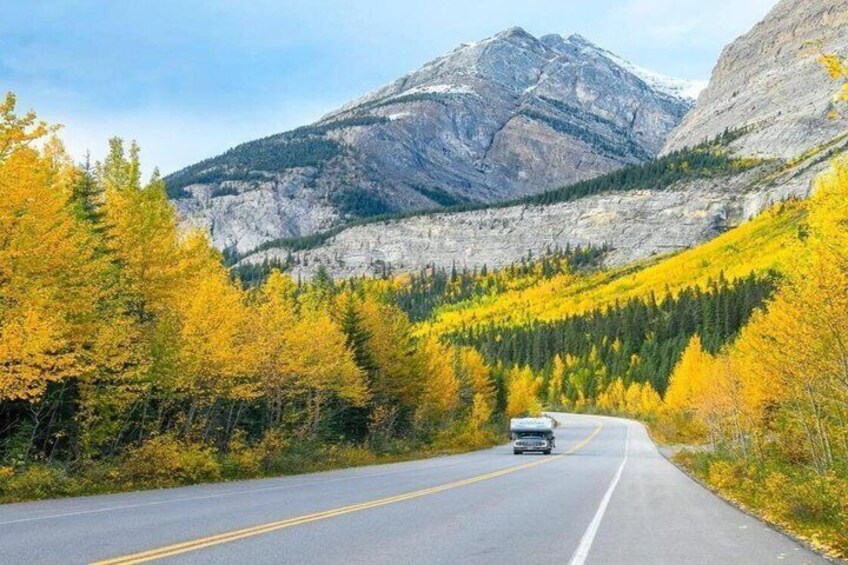 A mountain road with autumn foliage, a vehicle, and a clear sky. 3