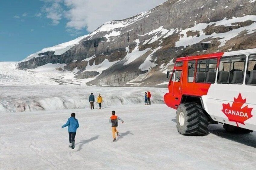 A red and white Canada bus on a snow-covered glacier with people walking around. 1