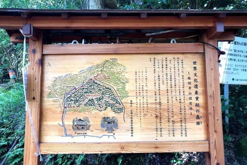 A wooden sign with a map and text, likely a tourist information board in a forested area. 2