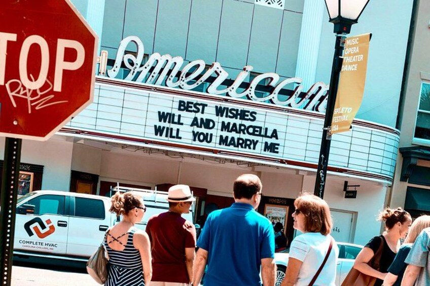A theater marquee with 'American' and a play title, a stop sign, and people walking outside. 4