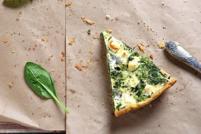 A slice of spinach and cheese quiche on parchment paper with a knife and a leaf. 3