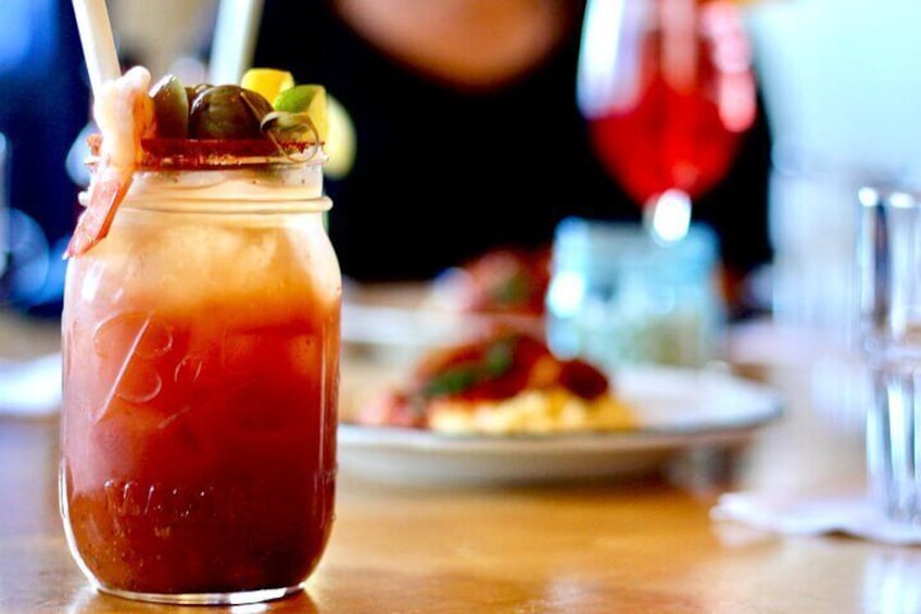 A glass jar with a red beverage, garnished with olives and lemon, on a wooden table. 3