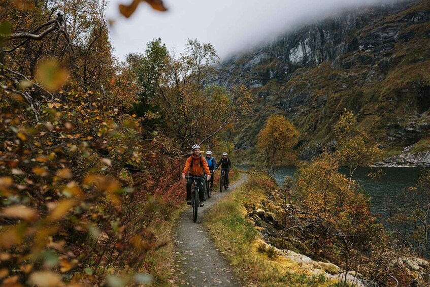 Three cyclists on a mountain path surrounded by autumn foliage and a lake. 3