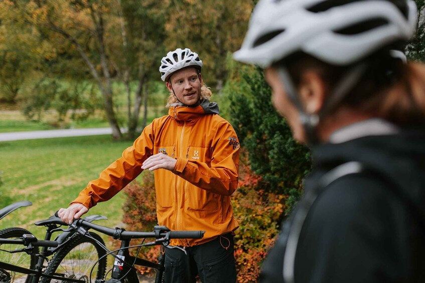 A person in an orange jacket and white helmet standing next to a bicycle. 1