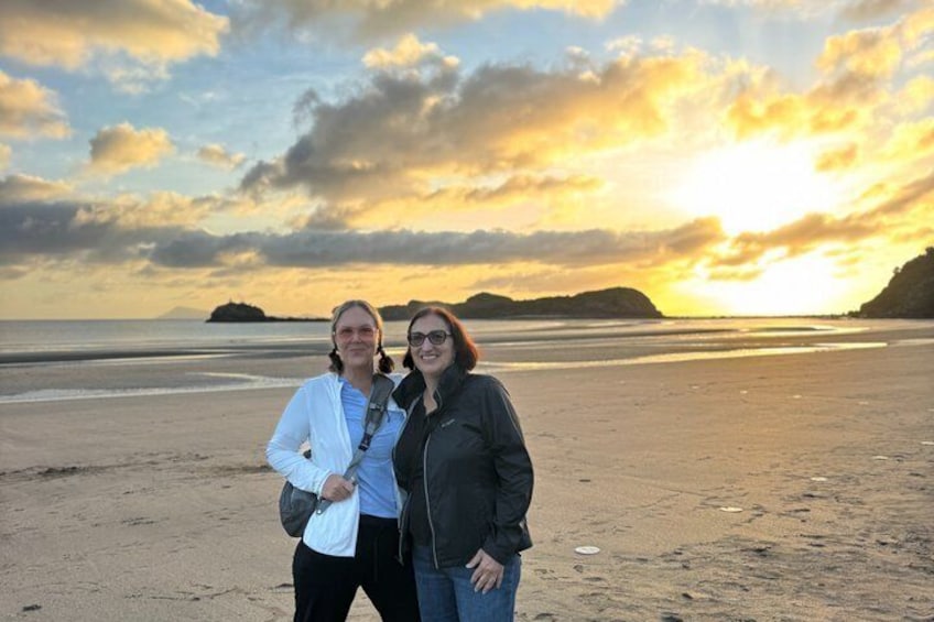 Two people standing on a beach with a sunset in the background. 5