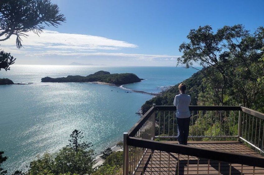 A person standing on a wooden deck overlooking a coastal landscape with clear blue water and distant landforms. 4