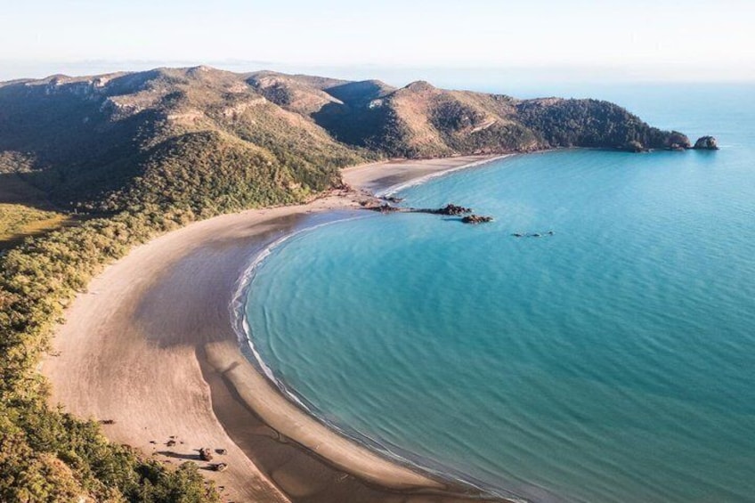 A coastal landscape with a sandy beach, clear turquoise waters, and rolling hills in the background. 3