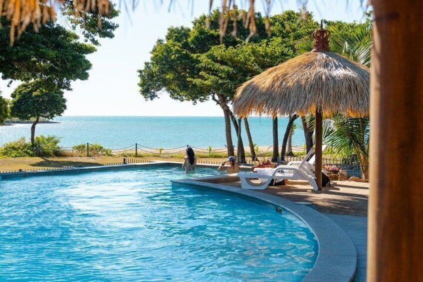 A swimming pool with lounge chairs, a thatched umbrella, and a view of the ocean. 3