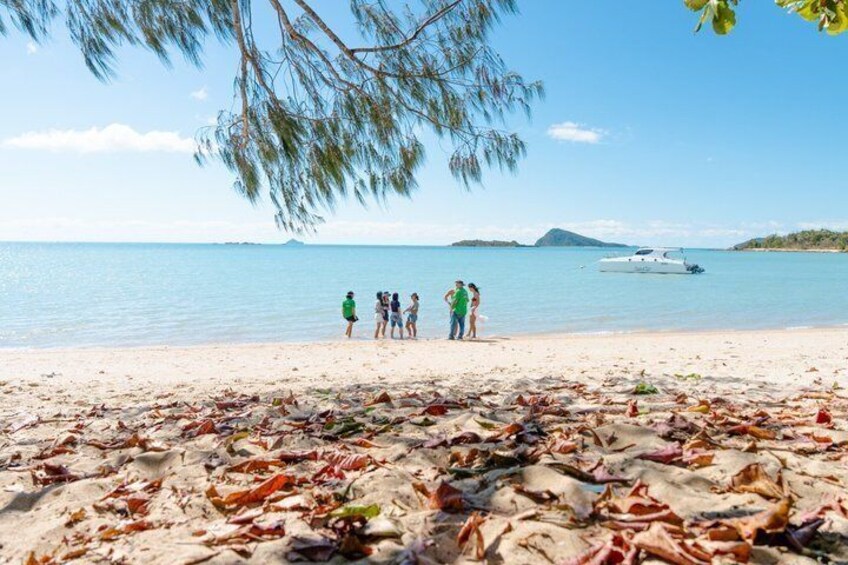 A beach with people standing, a boat in the water, and a clear sky. 1