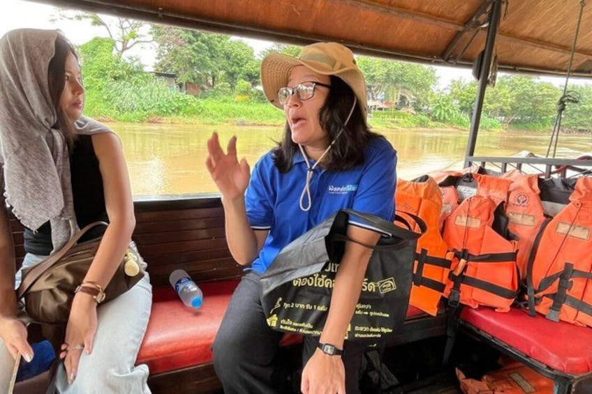 Two people on a boat, one wearing a blue shirt and a straw hat, and the other in a black top with a towel over their head. Life jackets are visible on the boat. 2