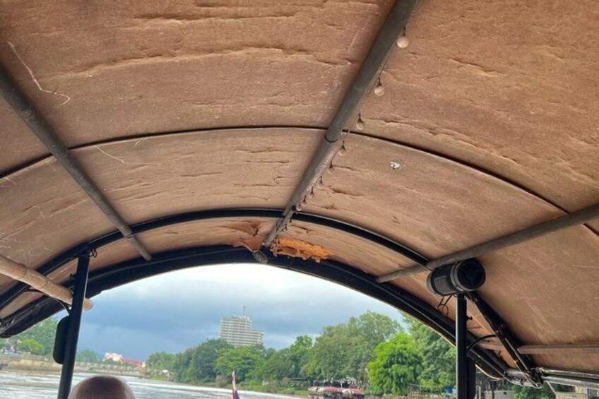 A covered area with a curved roof, metal beams, and a view of a river with buildings and trees in the background. 4