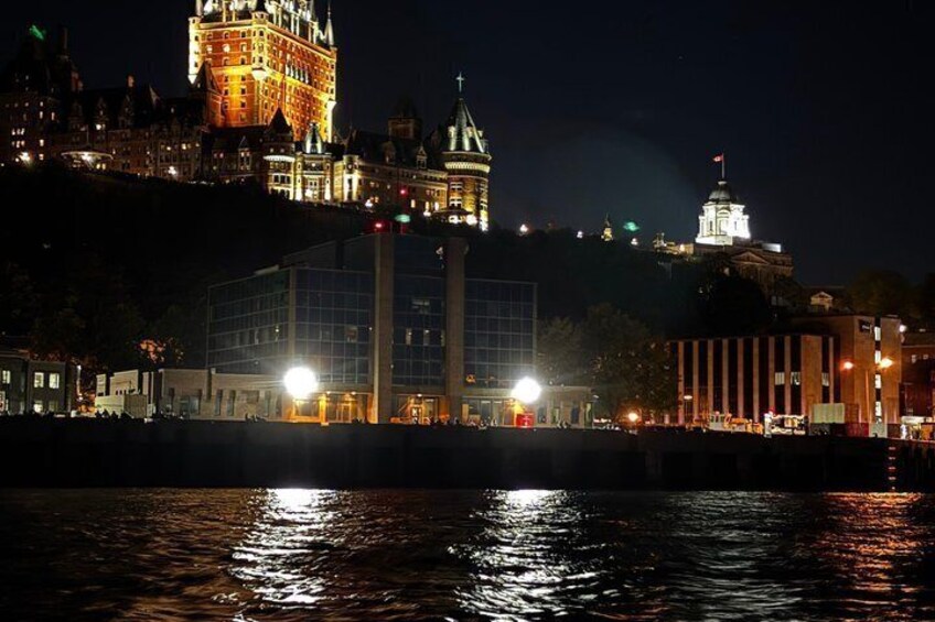 A nighttime cityscape with illuminated buildings, a river, and a hilltop castle. 3