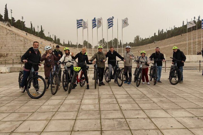 A group of people on bicycles in an outdoor setting with stone steps and flags in the background. 2