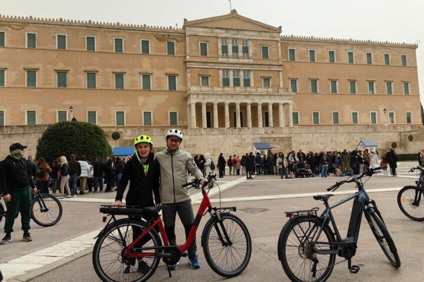 A group of people with bicycles in front of a large classical building. 3