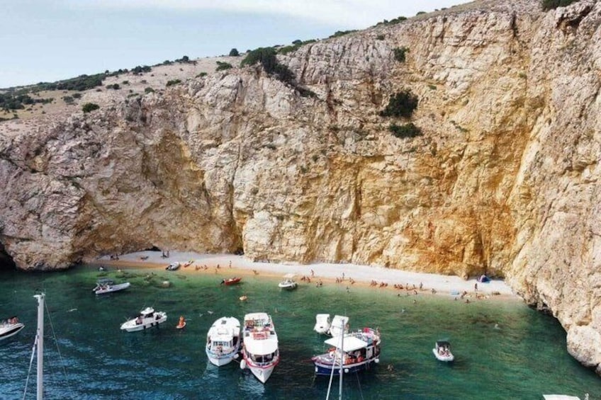 A coastal area with boats docked near a rocky cliff and a beach. 1