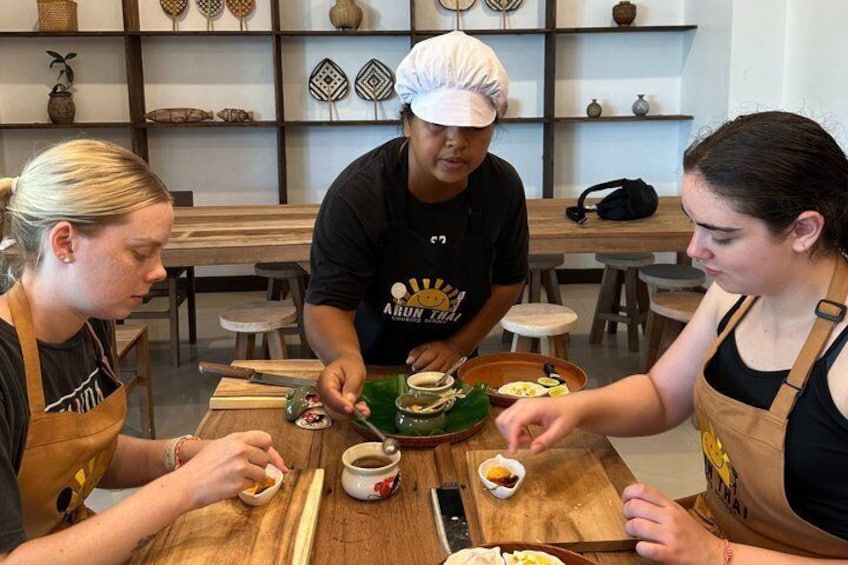 Three people preparing food at a wooden table with kitchen utensils and bowls. 2