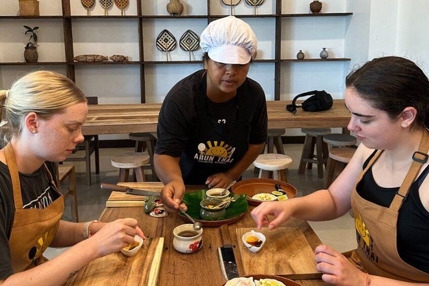 Three people preparing food at a wooden table with kitchen utensils and ingredients. 2