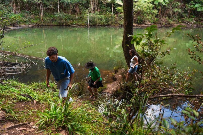 Three people near a pond surrounded by greenery. 4