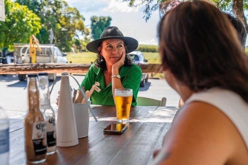 Two people sitting at an outdoor table with a beer glass, a bottle, and a pitcher. 2