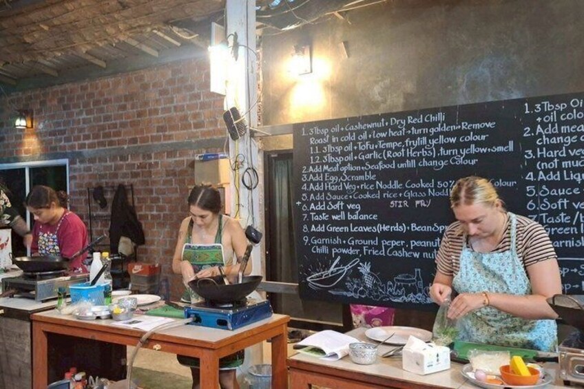 A cooking class with participants preparing dishes, a chalkboard with a recipe list, and cooking utensils on the table. 5