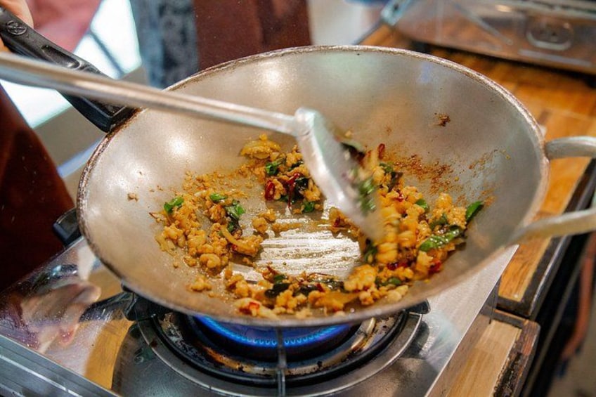 A wok on a stove with food being stirred. 1
