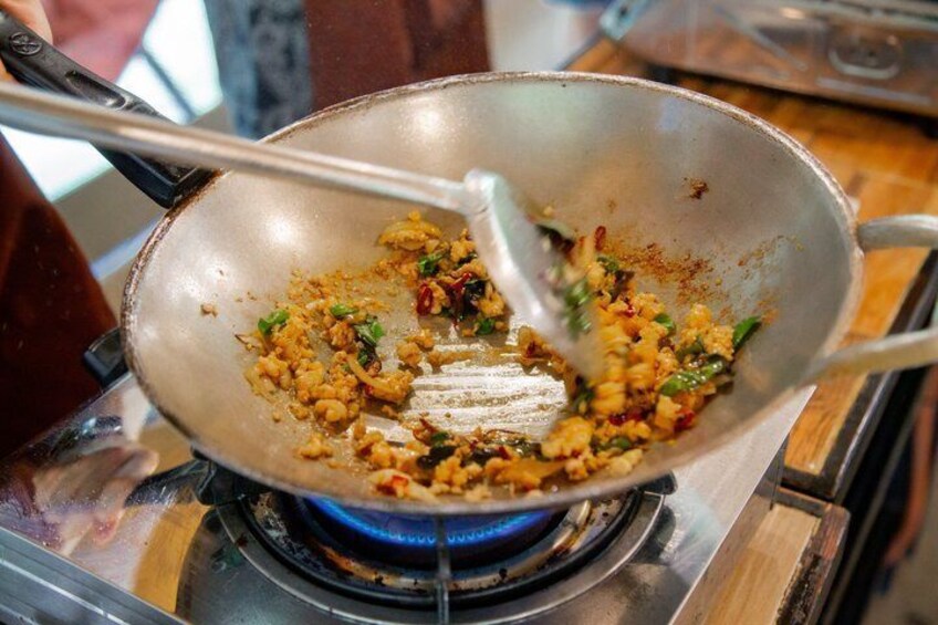 A wok on a stove with food being stirred. 1