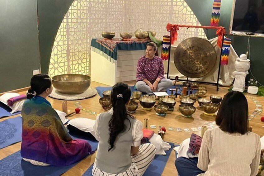 A group of people sitting on mats in a room with singing bowls and a large gong. 3