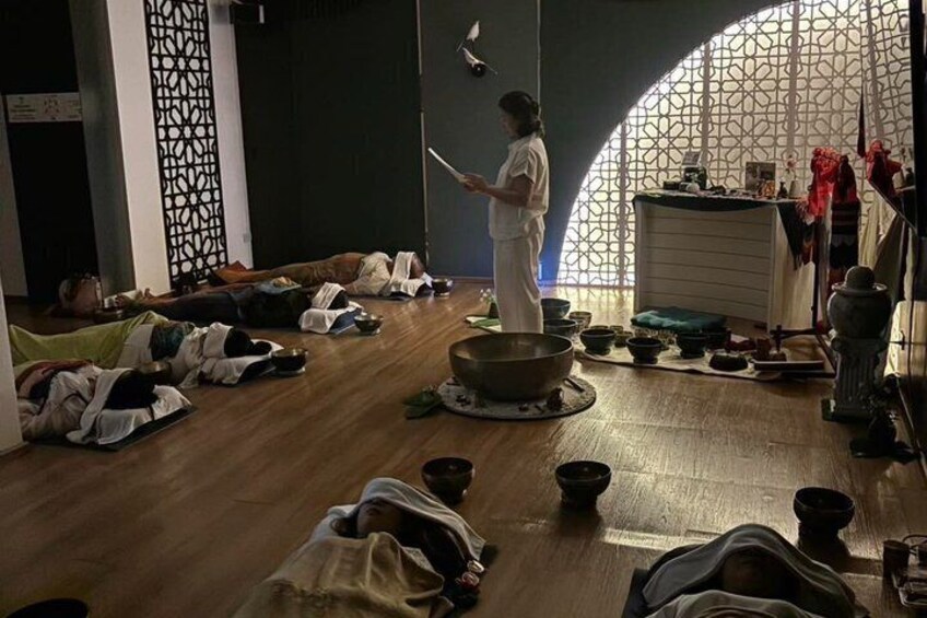 A person standing in a room with a large circular object on the floor, surrounded by people lying on mats. 2