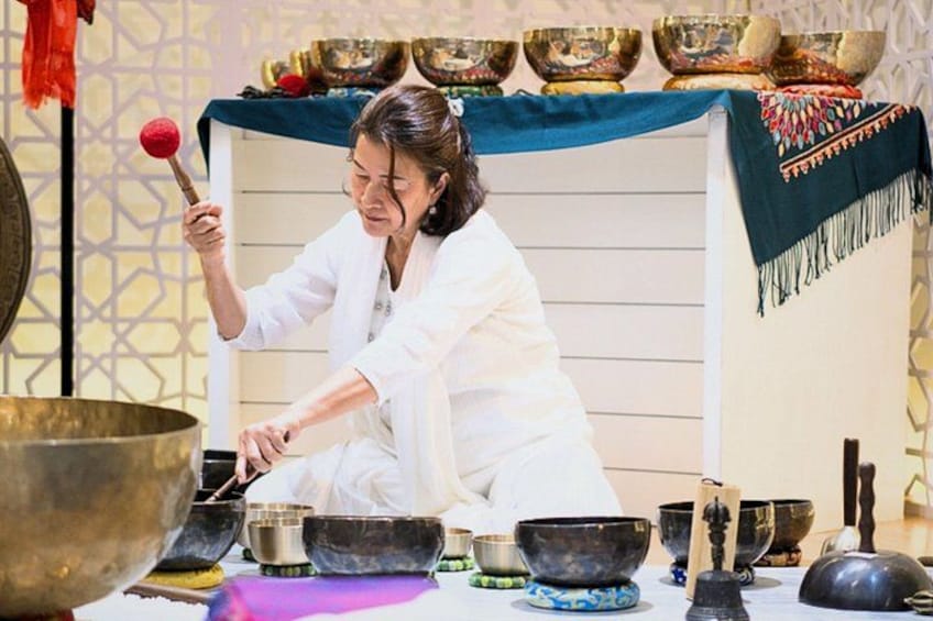 A person playing a traditional instrument, surrounded by various bowls and a large gong. 1