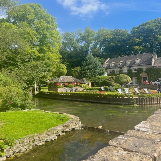 A riverside garden with a stone bridge, a stone building, and lounge chairs along the water. 2