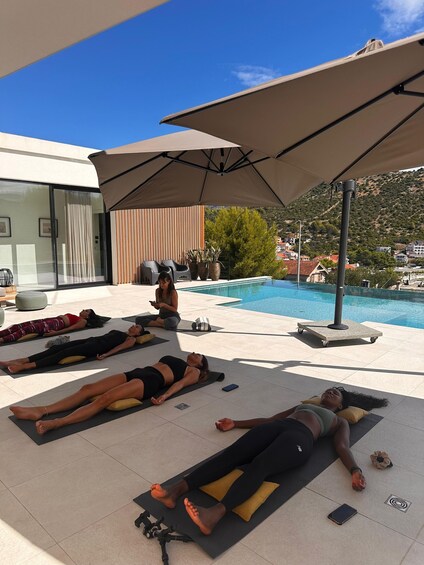 People sunbathing on mats by a pool with umbrellas. 4