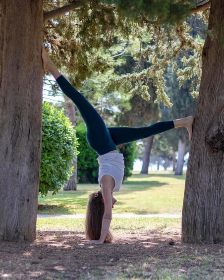 A person performing a handstand between two trees in a park. 2